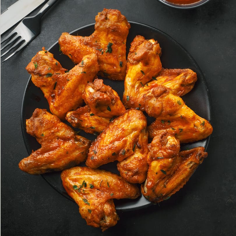 A black plate filled with La Pizzeria's spicy, glazed chicken wings, garnished with herbs.