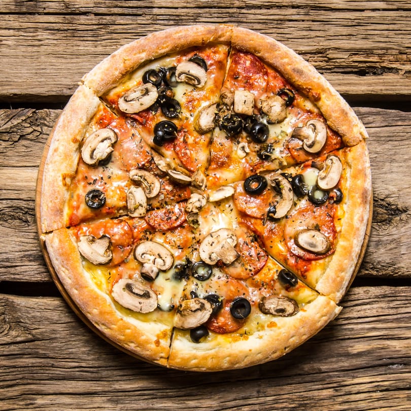 La Pizzeria's mushroom, olive, and pepperoni pizza, sliced on a rustic wooden table.