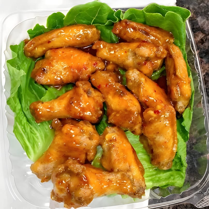 Sweet and spicy chicken wings on a bed of lettuce in a clear plastic container.