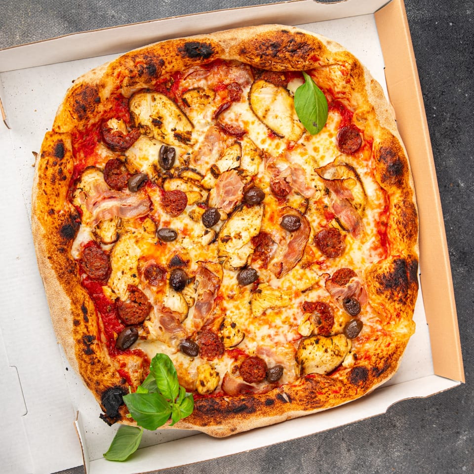 La Pizzeria's pizza with chicken, pepperoni, olives, and basil in a delivery box.